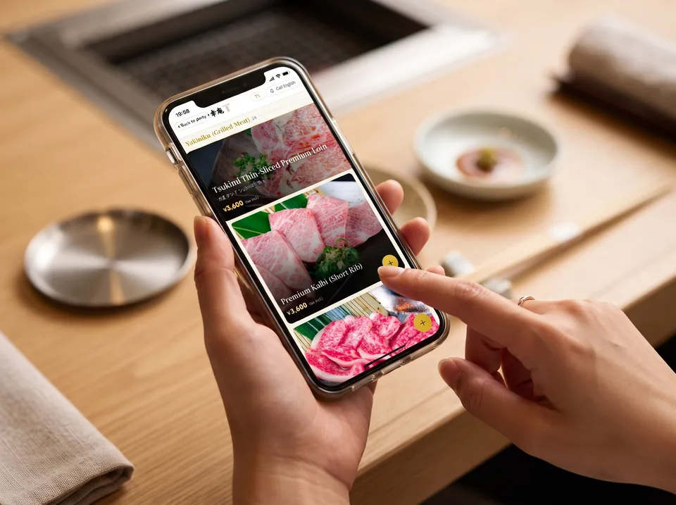 スマートフォンの英語メニューで料理を選ぶ手元(AI生成の利用イメージ)